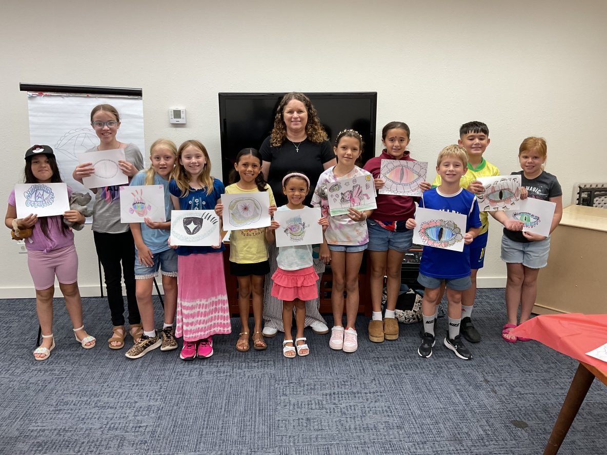 A group of children and an art teacher pose holding their pictures of dragon eyes that they drew