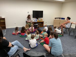 children sit in the library and listen to a story from the librarian.