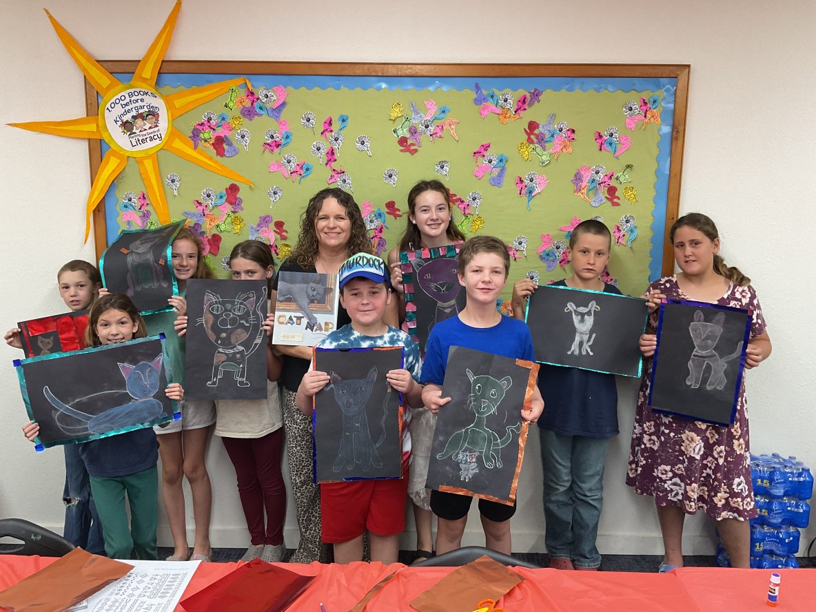 a group of children hold their artwork of cats in various poses and colors