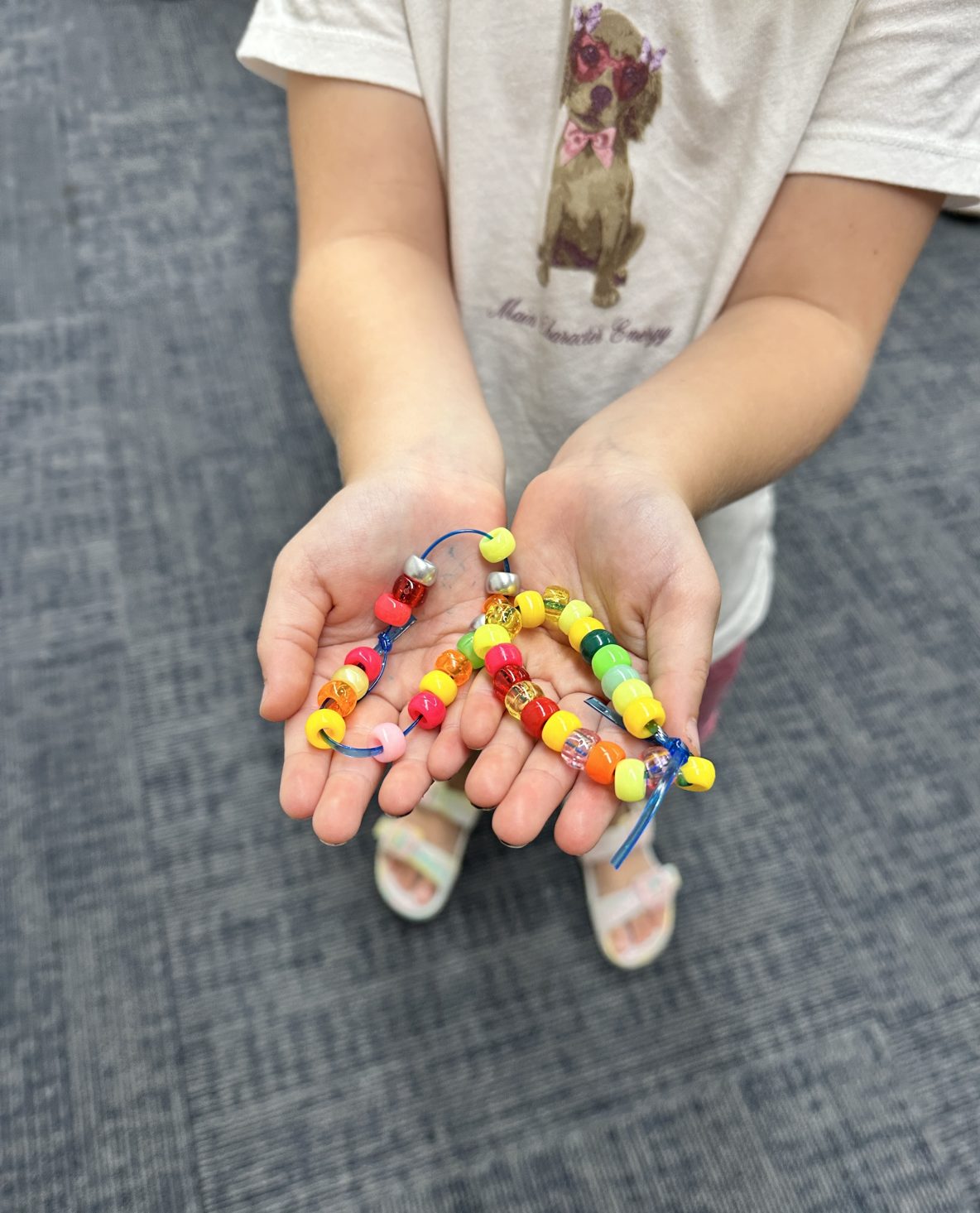 a little girl holds out two friendship bracelets made of colorful pony beads