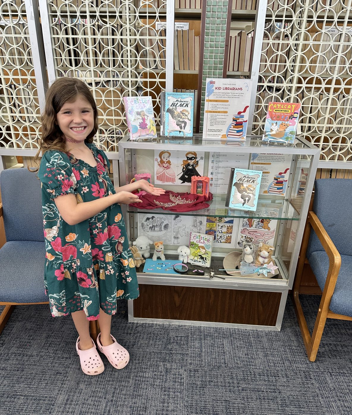 a girl stands next to a glass display case full of stuffed animals and other items that are from the books displayed