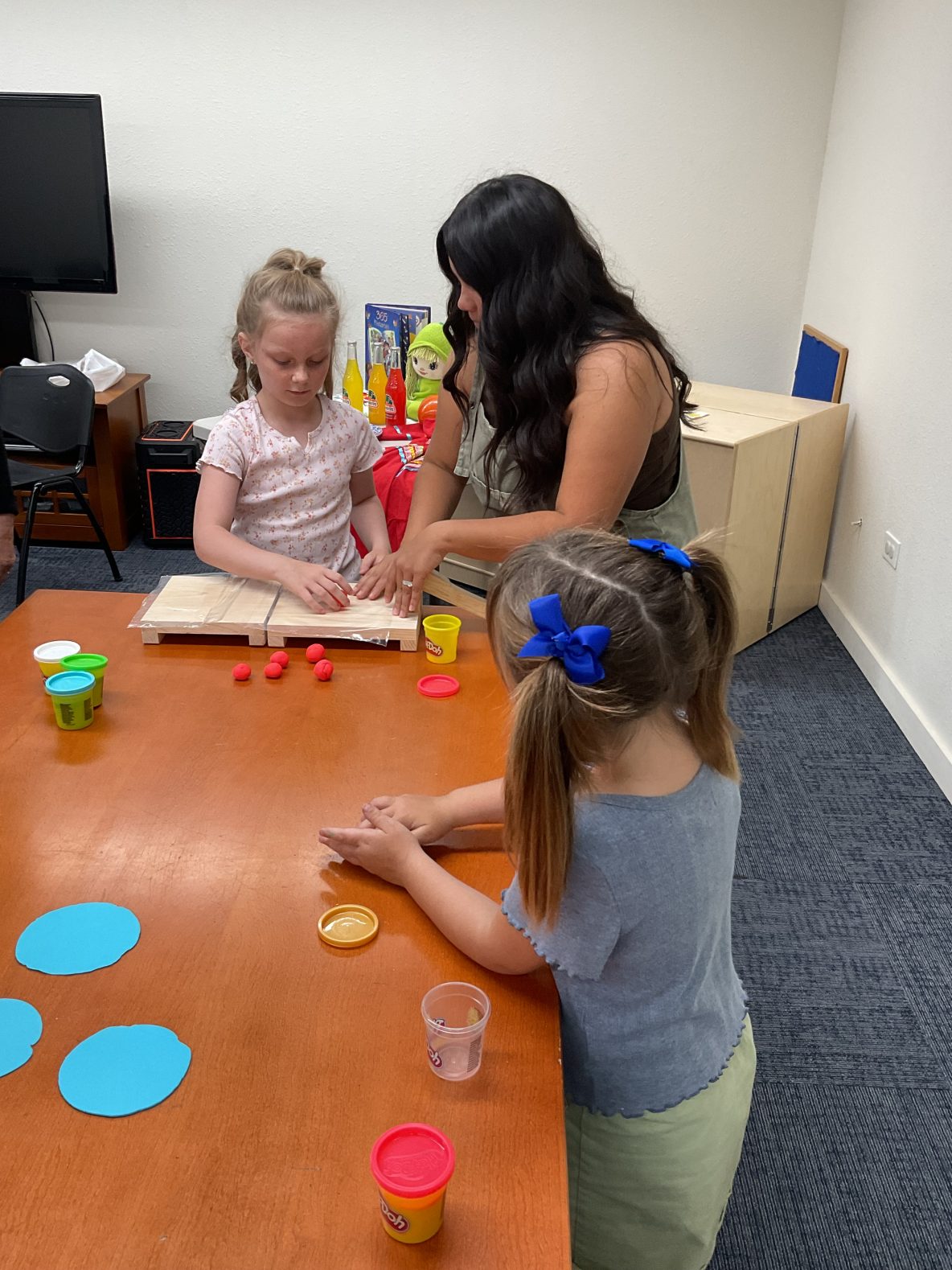 librarian helps a child make a play-dough tortilla using wooden tortilla press